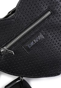 Borsa a mano in pelle nera perforata con zip argentata, caratterizzata da un patch con il logo DKNY. Include una tracolla staccabile per maggiore versatilità.