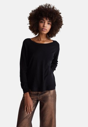 Maglione nero a maniche lunghe con scollo a spalle scoperte, realizzato in materiale morbido, abbinato a pantaloni ampi in bronzo metallizzato.