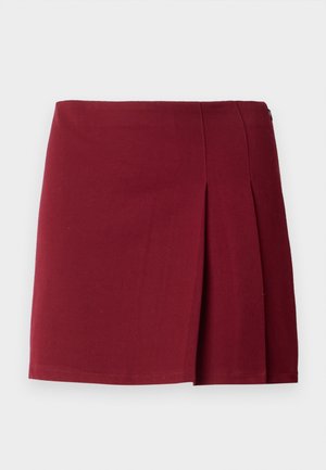 Jupe mini plissée bordeaux avec une texture lisse, taille ajustée et fermeture à glissière sur le côté. Design simple et minimaliste sans motifs.