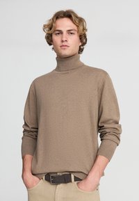 Maglione a collo alto di colore marrone chiaro, realizzato in tessuto morbido. Presenta maniche lunghe con polsini a coste e un design a collo alto.