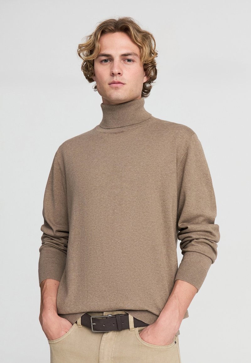 Maglione a collo alto di colore marrone chiaro, realizzato in tessuto morbido. Presenta maniche lunghe con polsini a coste e un design a collo alto.