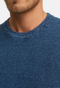 Pull en tricot bleu avec un col rond côtelé et un tissu texturé, avec un gros plan mettant en avant le détail des coutures et la forme du col.