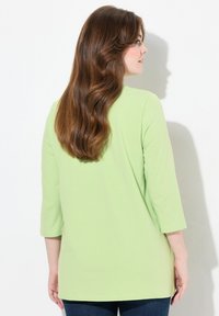 Muntgroene longsleeve top met een relaxte pasvorm, voorzien van een ronde halslijn en zijsplitten, gecombineerd met donkerblauwe spijkerbroeken.