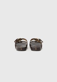 Sandalias de slide marrones con dos correas ajustables, hebillas doradas y una suela plana. Textura suave con un diseño minimalista.