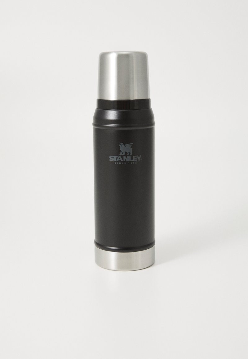 Black stainless steel thermos with a shiny silver lid and base, featuring a logo with a lion emblem. Smooth texture, cylindrical shape.