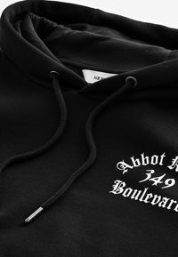 Sudadera negra hecha de tela suave, con capucha ajustable, puños acanalados y un diseño impreso en blanco con texto en fuente estilizada.