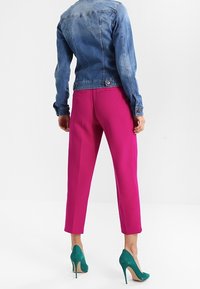 Chaqueta vaquera con diseño estructurado, color azul y detalles de botones. Combinada con pantalones cortos de color rosa intenso y zapatos de tacón alto verdes.