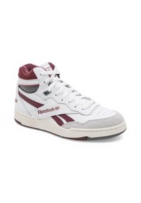 Biele vysoké tenisky s marhuľovými akcentmi, koženým zvrškom, polstrovaným golierom, okrúhlou špičkou a textúrovanou šedou gumovou podrážkou. Obsahujú branding Reebok.