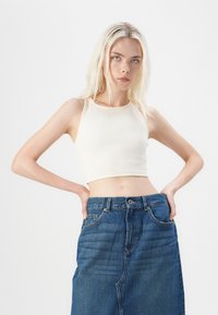 Cream ribbed crop top with a rounded neckline paired with a high-waisted denim skirt. The skirt features subtle texture and pockets.