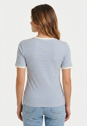 Femme aux longs cheveux bruns portant un t-shirt à manches courtes rayé blanc et bleu et un jean bleu clair, vue de dos.