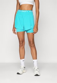 Svetle modré šortky Nike s elastickým pasem, s vrstveným designem. Nošeny s bílými ponožkami a teniskami, na neutrálním pozadí.