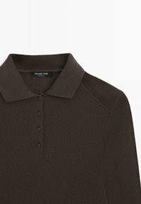 Dark brown polo shirt made of ribbed fabric. Features a classic collar, four-button placket, and suede accents on the shoulders.