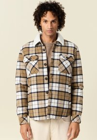 Giacca camicia a quadri marrone e bianca, con un morbido colletto bianco, due tasche sul petto con pattine e chiusure a bottoni.