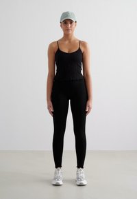 Svart ribbad linne med vågig nederkant, matchad med svarta leggings och vita träningsskor. Ljusblå keps fulländar outfiten.