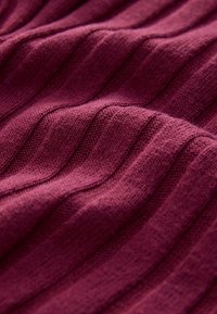 Tessuto in maglia bordeaux con texture a coste in rilievo, finitura morbida e lucentezza sottile. Presenta motivi ondulati sulla superficie.