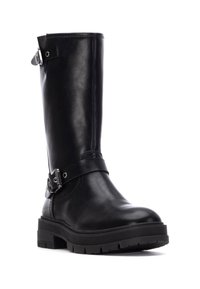 Bota de cuero negra hasta la rodilla con punta redonda, suela de goma gruesa y una correa ajustable con un detalle de hebilla de plata en el tobillo.