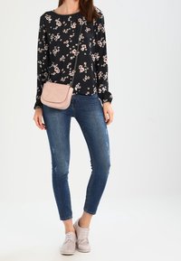 Blouse à manches longues noire à fleurs, jean skinny bleu et sac bandoulière rose clair. Les chaussures sont roses claires et à lacets.