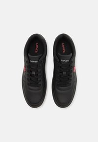 Zapatillas de piel negras con punta redonda, patrón texturizado y perforaciones. Cuentan con cordones negros y el logo rojo de Levi's en la lengüeta y el costado.