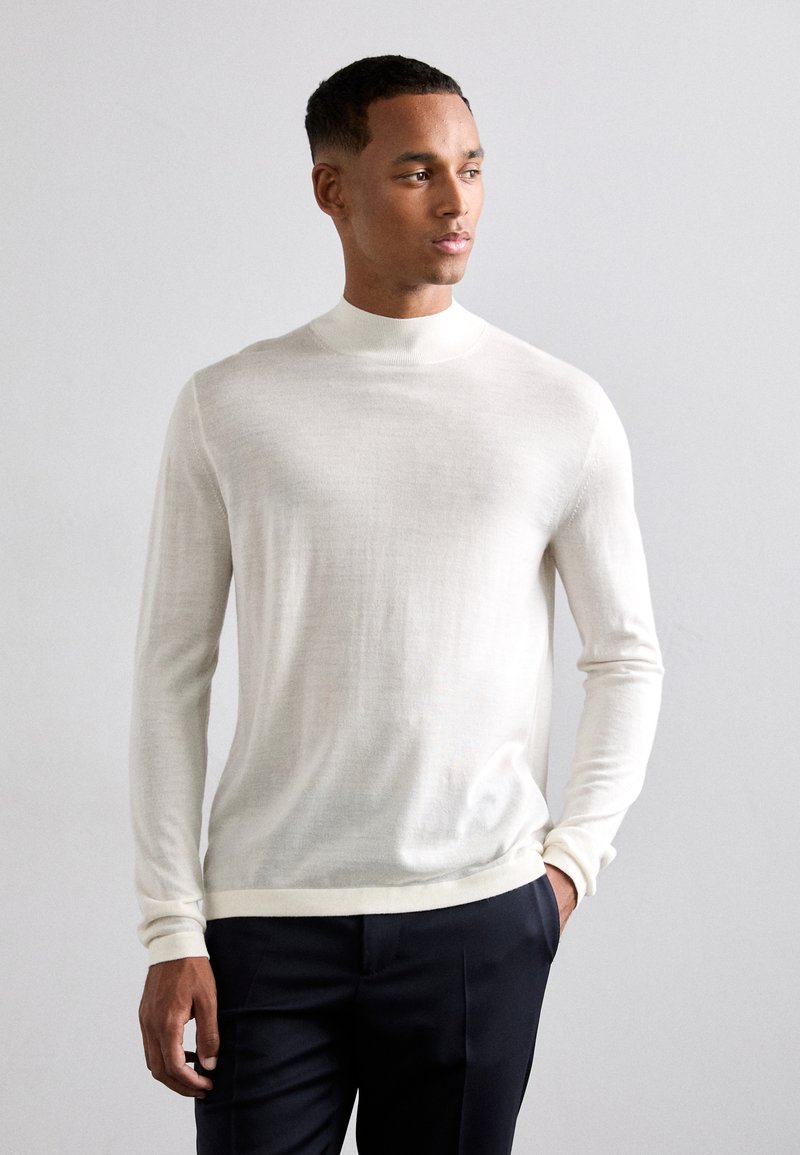 Maglione leggero di colore crema a maniche lunghe con collo alto, realizzato in tessuto morbido, con una vestibilità rilassata e polsini a coste.