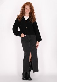 Schwarze gestrickte Strickjacke mit V-Ausschnitt und fünf goldenen Knöpfen, kombiniert mit einem schwarzen Denim-Rock mit Schlitz vorne und kniehohen schwarzen Stiefeln.