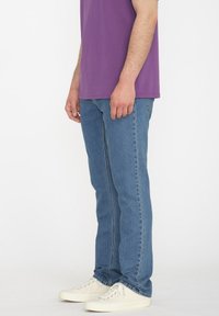 Jeans de denim azul claro con corte recto, combinados con una camiseta de algodón morada y zapatillas blancas, vistos de lado.
