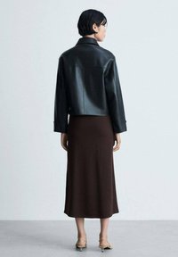 Jachetă scurtă din piele neagră, rochie midi maroniu și sandale bej cu barete. Textură netedă, design minimalist și paletă de culori neutră.