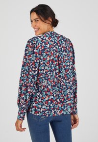 Blusa floral azul marino de manga larga, con un vibrante patrón de flores rojas, rosas y en tonos verdosos. Tejido suave con un corte holgado y espalda fruncida.