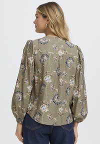 Roheline lillemustriga pluus pahteldatud varrukate ja kummist mansettidega. Omadused: tekstureeritud kangas kreemika ja sinise lillemustriga. Klassikaline tagumine disain.