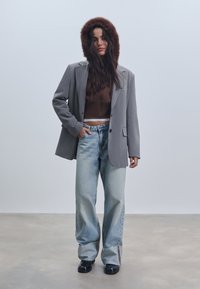 Sivi blejzer s umjetnim krznenim kapuljačom, smeđi kratki top, svijetloplave široke traperice i crne chunky cipele. Glatke teksture, ležeran kroj.