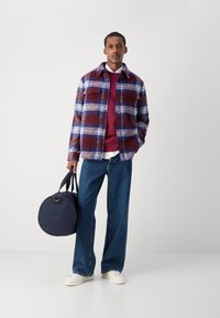 Plaid jacket in burgundy, blue, and white; layered over a maroon sweatshirt; paired with wide-leg blue jeans and a round navy bag.