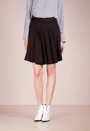 Donna con gonna nera plissettata, camicia a righe blu e bianca a manica lunga e stivaletti bianchi con zip frontali.
