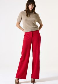 Pull court beige en peluche à manches courtes associé à un pantalon rouge large à taille haute et à texture. Des chaussures métalliques brunes complètent le look.