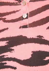 Chemise en coton rose avec un motif de rayures de zèbre brun foncé, dotée de trois boutons au col pour la fermeture.