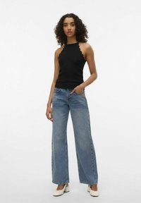 Top halter in maglia nera con bordi smerlati, abbinato a jeans a gamba larga blu chiaro e scarpe con tacco a blocco bianche.