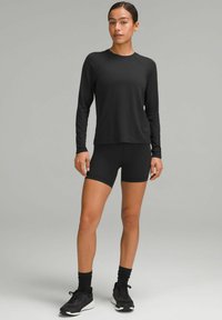 Crna dugosleeve atletska majica s okruglim izrezom, u kombinaciji s crnimŠortsevima. Glatka, rastezljiva tkanina; prilagodljiv dizajn; nosi se s crnim atletske obuće.