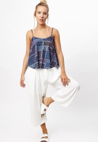 Top sin mangas de estampado navy con tirantes ajustables y corte holgado, combinado con pantalones anchos blancos y sandalias blancas.