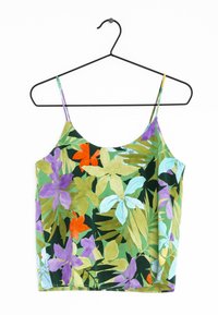 Débardeur à fleurs à fines bretelles ; motifs botaniques verts, violets, orange et bleus sur un tissu doux ; suspendu à un cintre en fil noir.