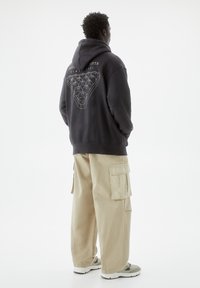 Sudadera con capucha gris con un gran gráfico en la parte posterior, combinada con pantalones cargo beige que cuentan con bolsillos laterales y un corte relajado.