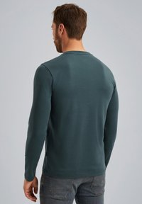 Langærmet skjorte i teal med rund hals og tætsiddende design. Lavet af blødt materiale med subtile sømme og uden synlige mønstre eller hardware.
