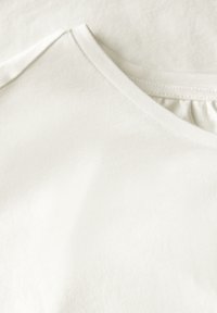 Weißes Baumwoll-T-Shirt mit V-Ausschnitt, weicher Textur und dezentem Rippenmuster entlang des Kragens. Glatte Oberfläche ohne Muster oder Verzierungen.