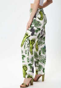 White wide-leg pants with a vibrant green and black tropical leaf and bird pattern. Made from lightweight fabric, featuring a high waist design.