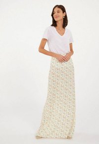 Jupe maxi en tissu léger, fond crème avec un petit imprimé floral coloré. Associée à un t-shirt ajusté blanc à col en V.