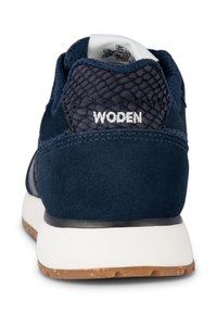 Marinblå sneakers med mocka och mesh-material, texturerad häl, vit "WODEN"-logotyp, vit mellansula och sula i gummi.