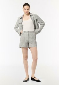 Grau karierter Blazer und Shorts-Set, aus strukturiertem Stoff gefertigt. Verfügt über einen Kragen, eine Knopfleiste und ein minimalistisches Design. Schwarze Ballerinas ergänzen das Outfit.