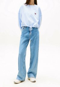 Sudadera corta de color azul claro con cintura ajustable y logo. Jeans de tiro alto de color azul claro con un ajuste holgado. Zapatillas blancas.