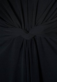 Schwarzer Stoff mit einem gerafften, gefältelten Design auf der Rückseite, das in der Mitte mit einem gedrehten KnotenDETAIL gebunden ist. Weiche, glatte Textur.