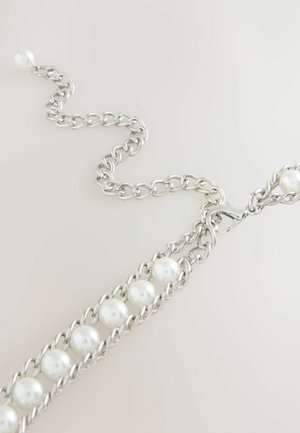 Bracciale in argento con perle bianche intrecciate e chiusura a moschettone su uno sfondo neutro chiaro.