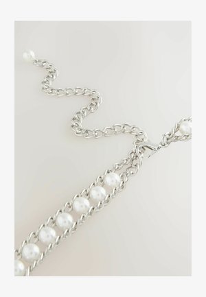 Bracelet en chaîne argentée avec des perles blanches entrelacées et un fermoir mousqueton sur un fond neutre clair.