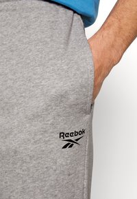 Grå bomullssweatpants med en svart Reebok-logotyp. Designad med en sidoficka och en avslappnad passform. Mjuk textur och enkel design.