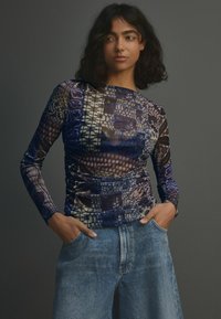 Top à manches longues en tissu léger et à motifs dans des nuances de bleu et de violet, avec des détails de fronces et un col rond.